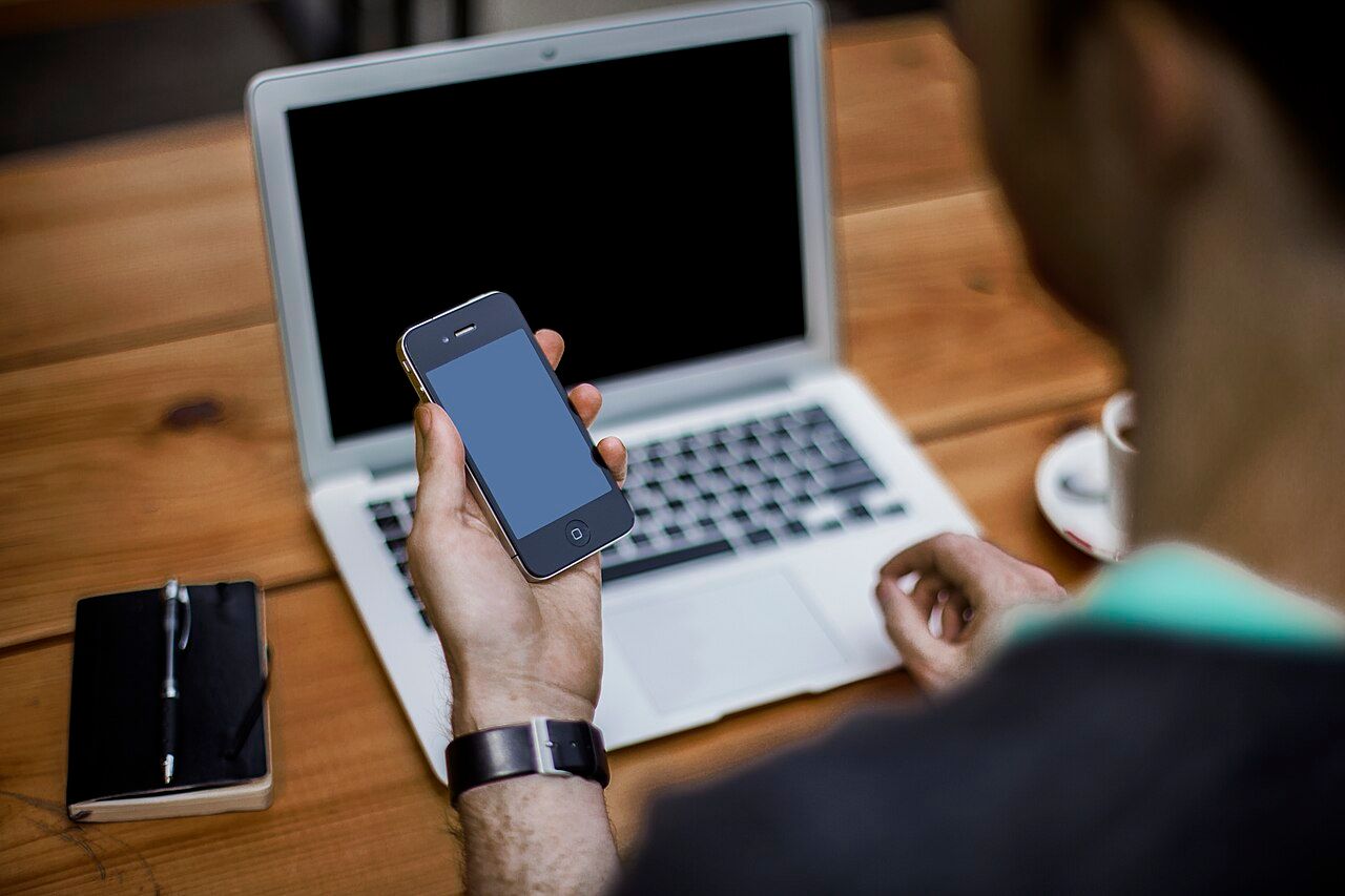 Person holding a phone at a laptop