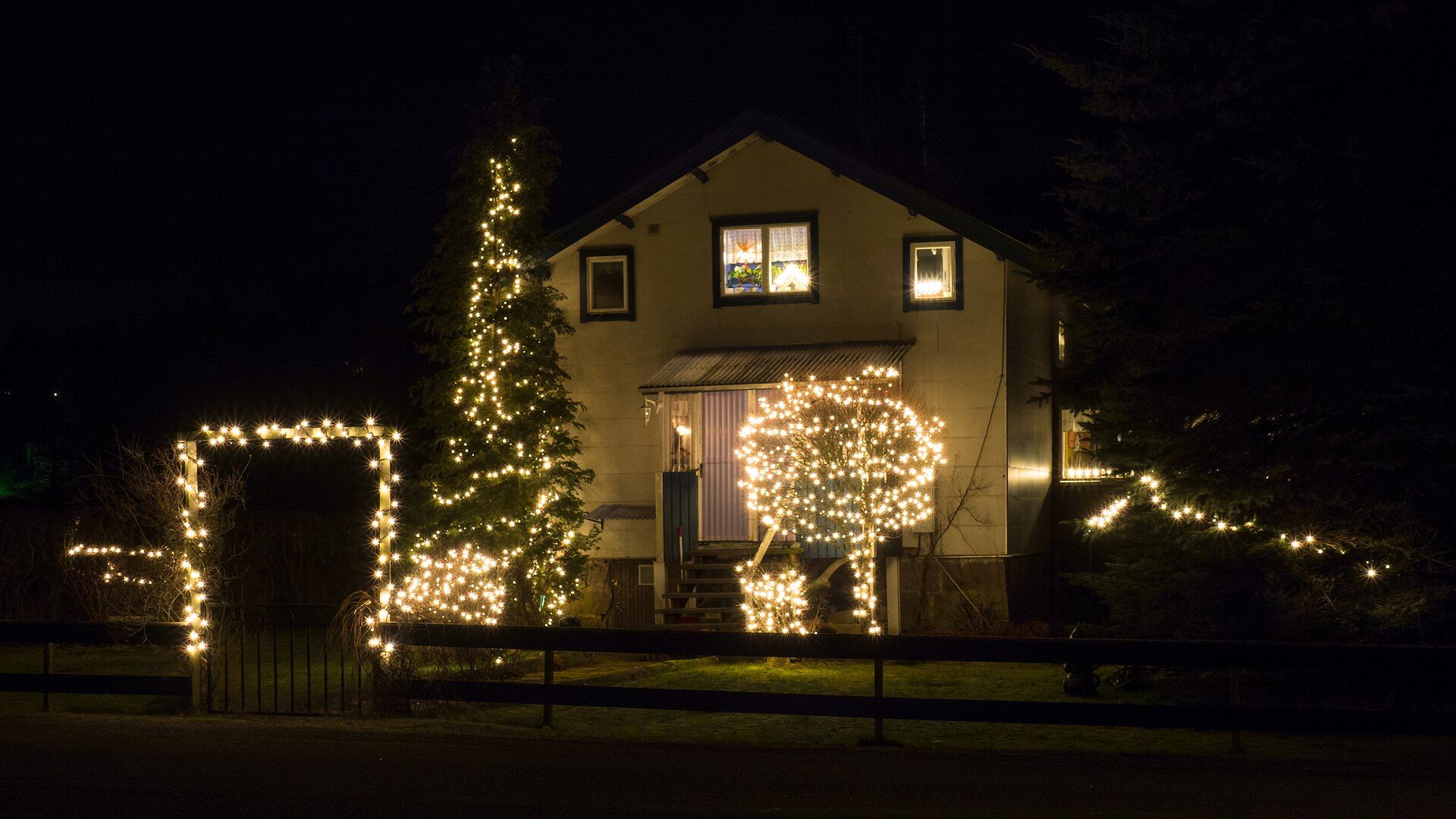 House with a lit tree, glowing bushes and a light arch